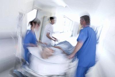 A motion blurred photograph of a senior female patient on stretcher or gurney being pushed at speed through a hospital corridor by doctors & nurses to...-stock-photo